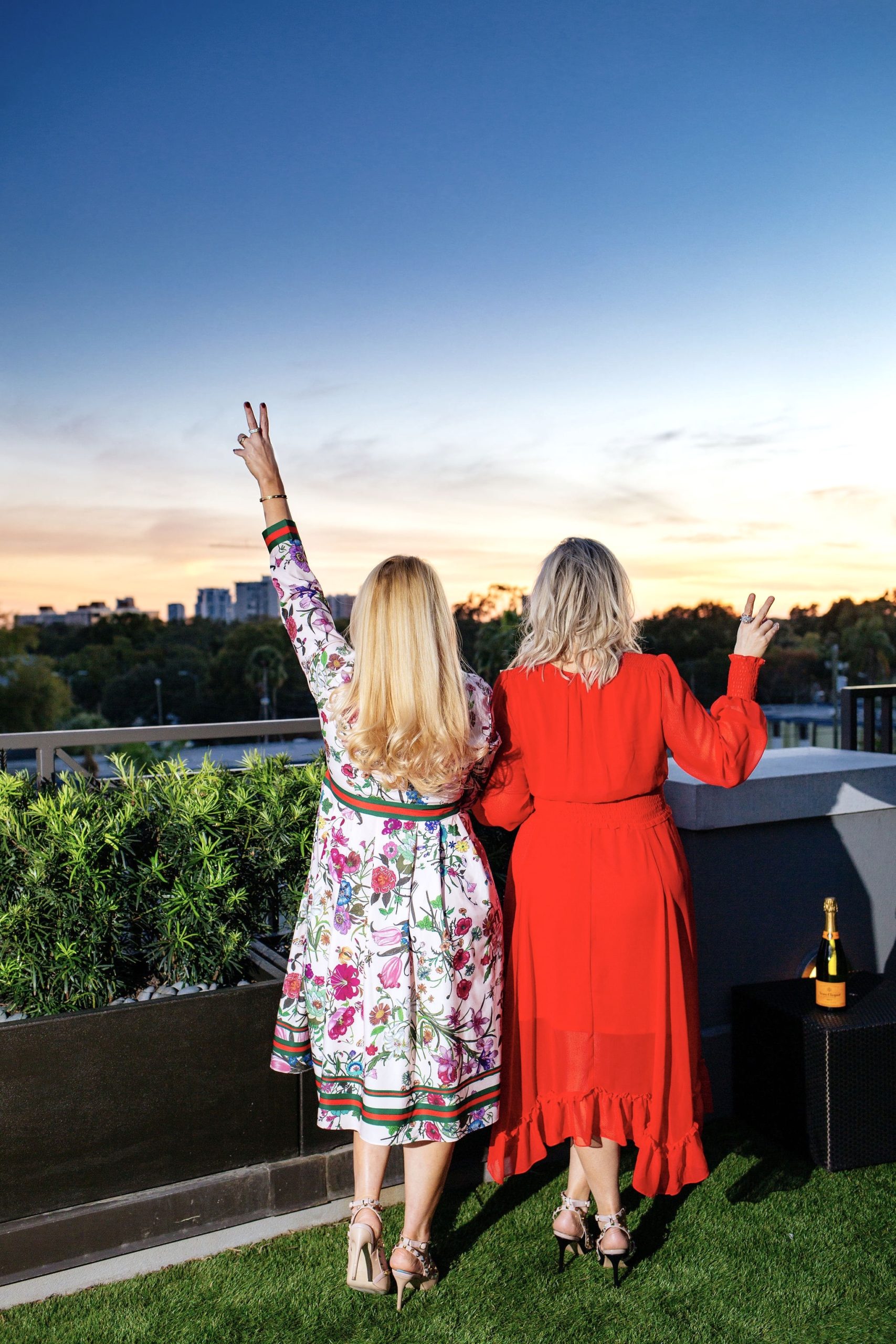 Jenn Truman Fashion and Style Blogger @jtstjtst11 is standing admiring the beautiful sunset skyline at Edge Rooftop Cocktail Lounge Epicurean Hotel, Autograph Collection. She is wearing a pink floral dress from amazon fashion and nude studded heels from amazon. She's holding the peace sign up with her first two fingers admiring the sunset.