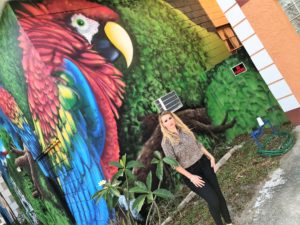 Woman standing by colorful parrot mural.