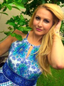 Woman in blue dress near green leaves.