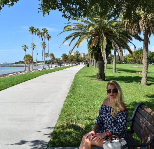 Woman sitting on bench by palm trees.