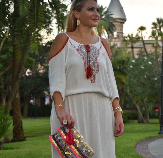 Woman in white dress holding colorful clutch.