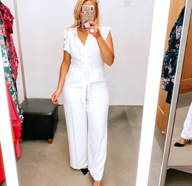 Tampa Blogger Jenn Truman providing a mirror selfie inside Nordstrom at Tampa International Plaza. She is wearing a CECE white jumpsuit from Nordstrom and Valentino dupe black studded heels from Amazon. She is holding her phone for a mirror selfie.